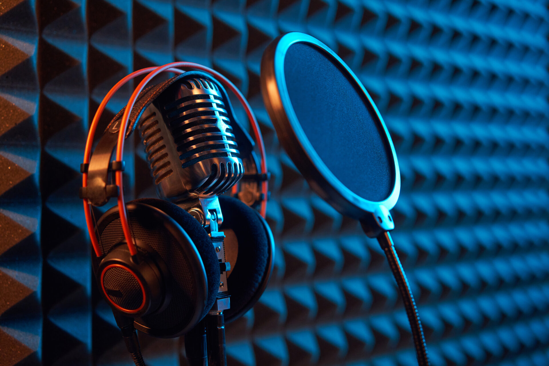 Studio condenser microphone with professional headphones and pop-up filter, on acoustic foam panel background with orange side light, copy space on right